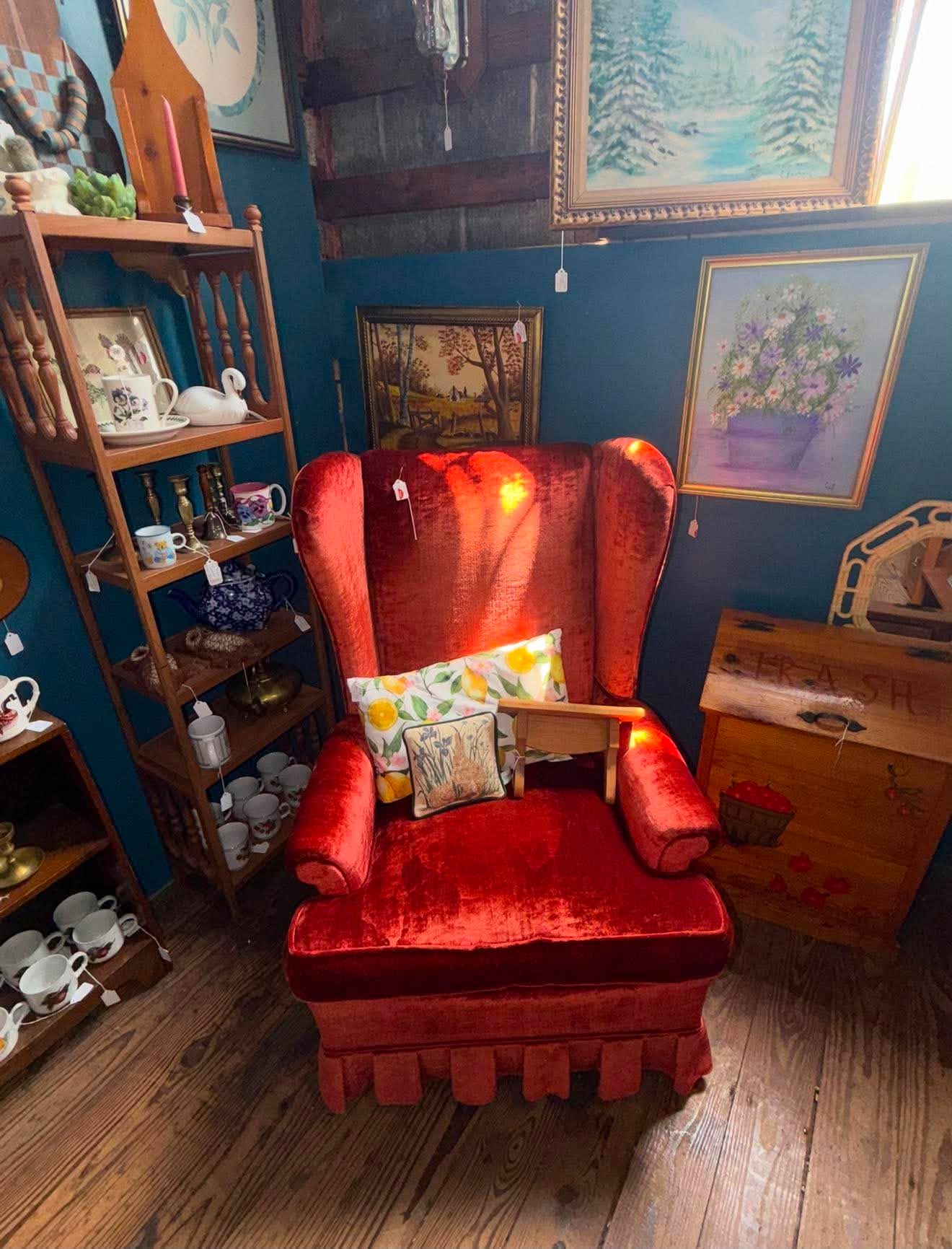 A bright red vintage wingback chair surrounded by framed art and teacups